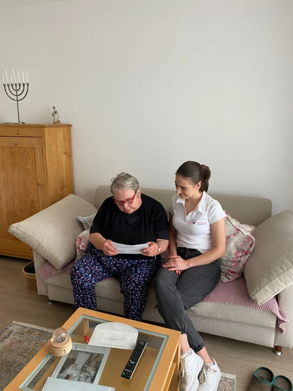 Mitarbeiterin der Daheim Agentur GmbH sitzt mit Seniorin zuhause und schaut gemeinsam Unterlagen an